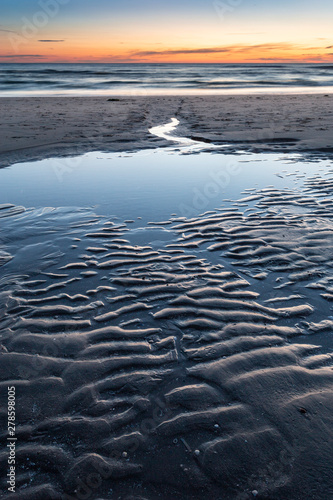 Beach after sunset during twilight. Water running from the beach to the sea with beautiful patterns in the sand.