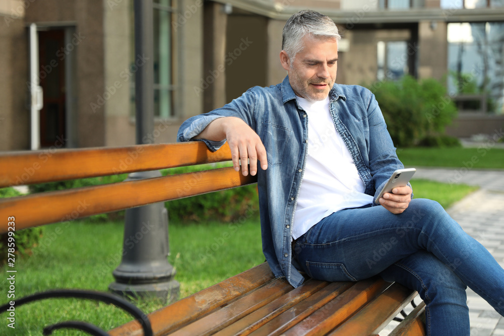 Fototapeta premium Portrait of handsome mature man using mobile phone in city. Space for text
