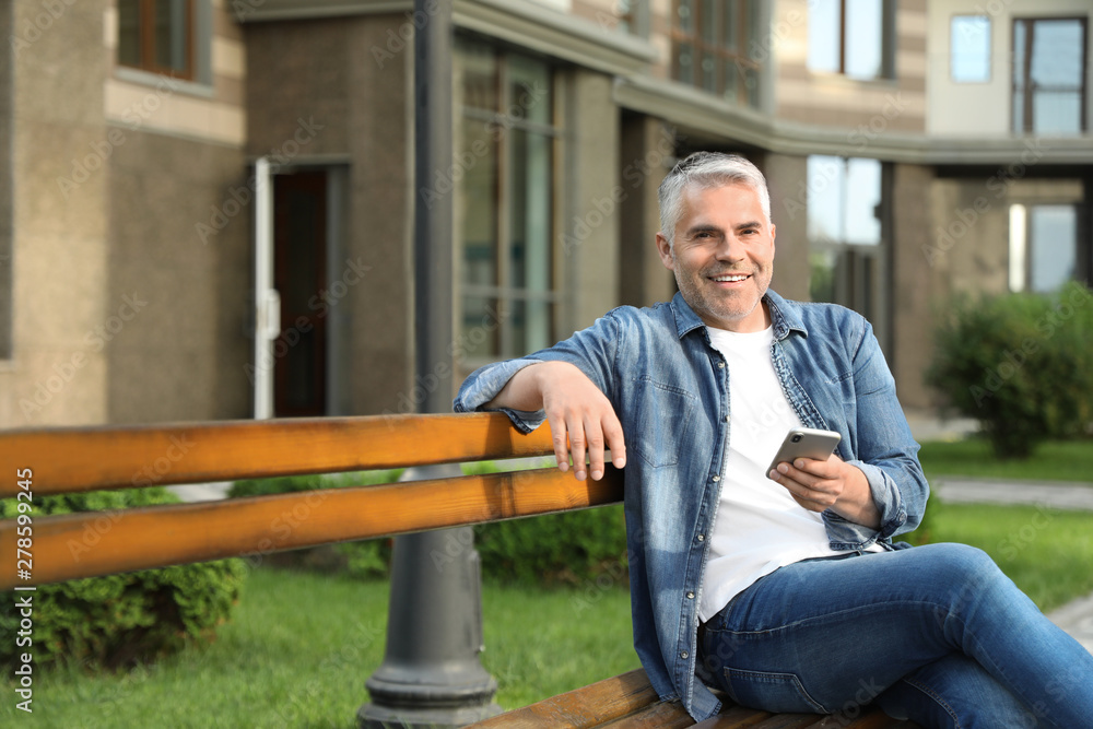Fototapeta premium Portrait of handsome mature man using mobile phone in city. Space for text