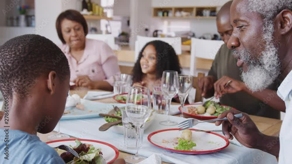 Multi-Generation Family Sitting Around Table At Home Enjoying Meal Together Multi-Generation Family Sitting Around Table At Home Enjoying Meal Together