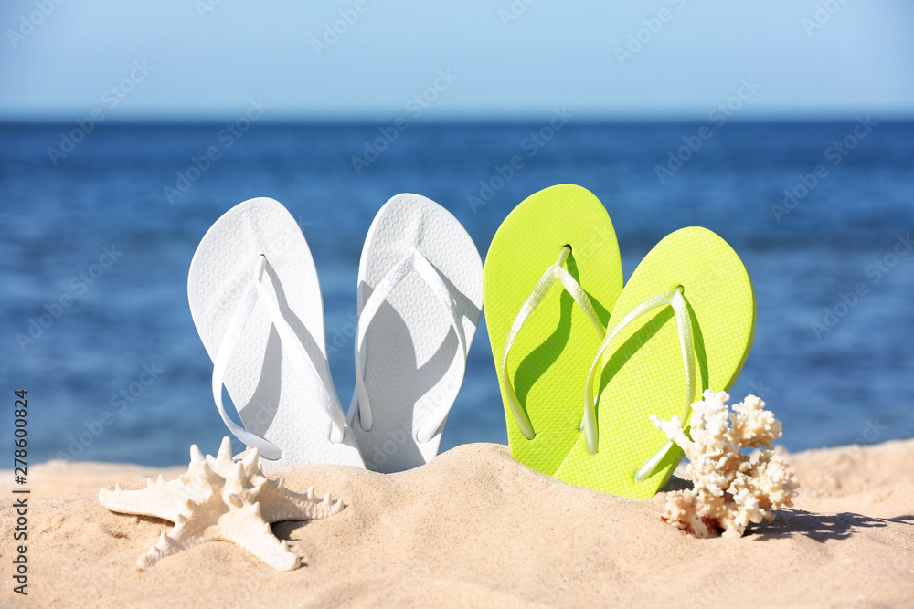 Composition with bright flip flops on sand near sea in summer. Beach accessories Composition with bright flip flops on sand near sea in summer. Beach accessories