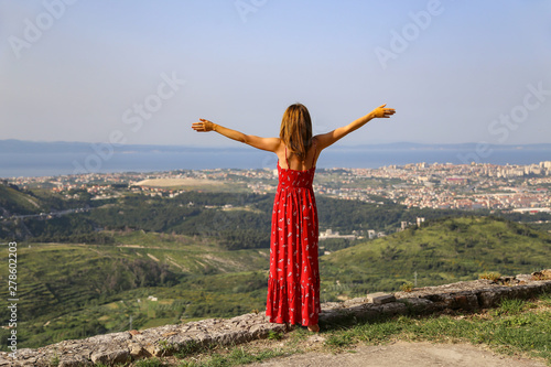 A girl with open arms stands on the edge of a cliff