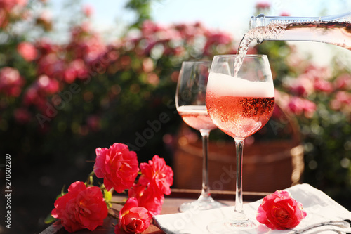 Pouring wine into glass on table in blooming rose garden. Space for text