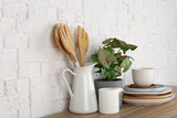 Green plant and different kitchenware on table near brick wall. Modern interior design