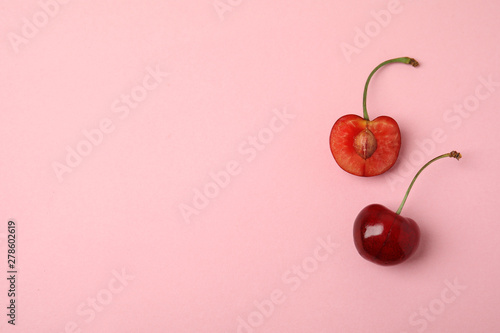 Cut and whole sweet cherries on pink background, top view. Space for text