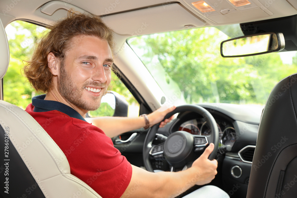 Attractive young man driving his luxury car, view from backseat Attractive young man driving his luxury car, view from backseat