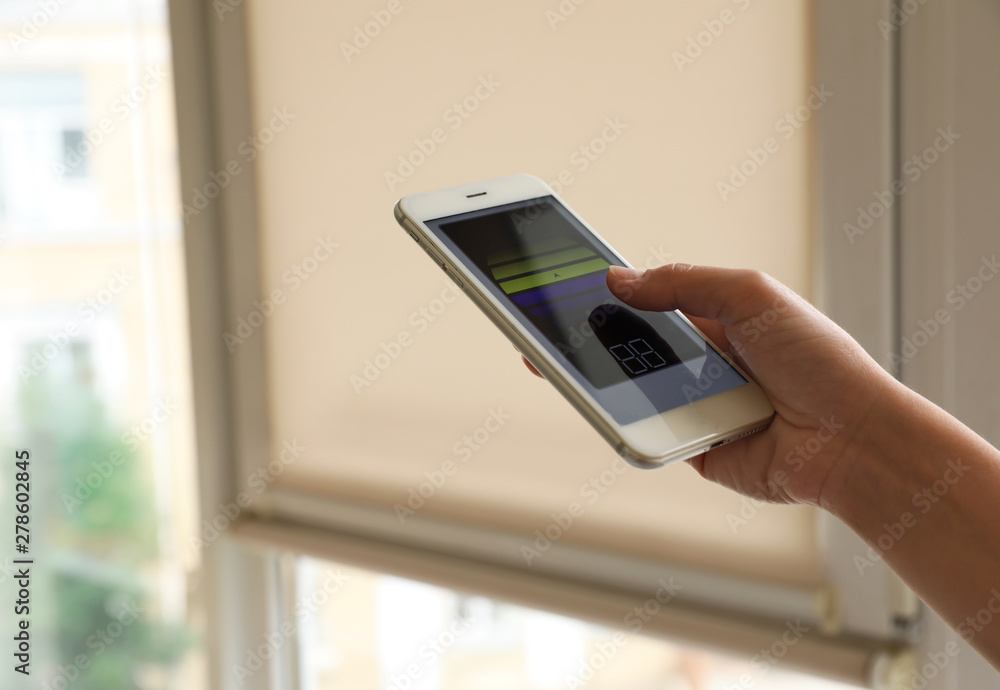Woman using smart home application on phone to control window blinds indoors, closeup. Space for text Woman using smart home application on phone to control window blinds indoors, closeup. Space for text