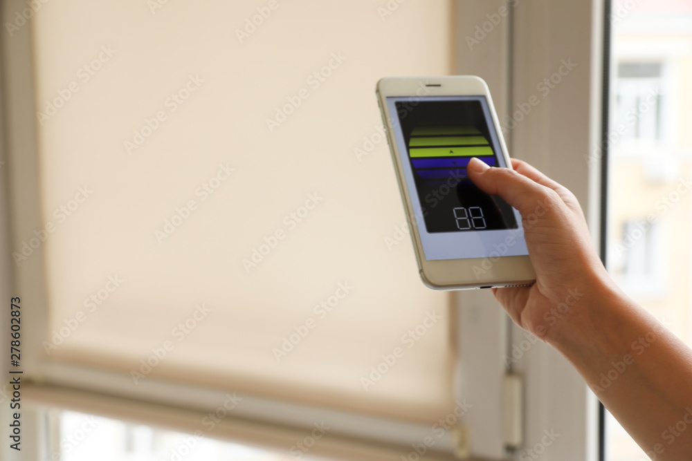 Woman using smart home application on phone to control window blinds indoors, closeup. Space for text Woman using smart home application on phone to control window blinds indoors, closeup. Space for text