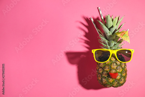 Funny face made of pineapple, sunglasses and strawberry slice with cocktail umbrella on pink background, top view. Space for text