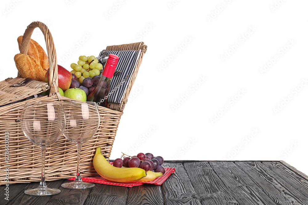 Wicker picnic basket with wine and different products on wooden table against white background, space for text Wicker picnic basket with wine and different products on wooden table against white background, space for text
