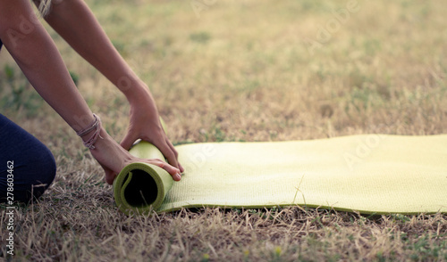 Cropped image of girl rolling yoga mat. Close-up of attractive young woman folding green yoga or fitness mat after working out in a glade in the woods or a city Park . Healthy life