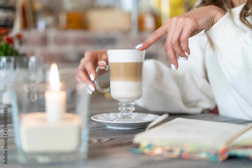 girl holding glass of latte coffee. candle is burning nearby and notepad is lying. Relaxed pastime concept girl holding glass of latte coffee. candle is burning nearby and notepad is lying. Relaxed pastime concept