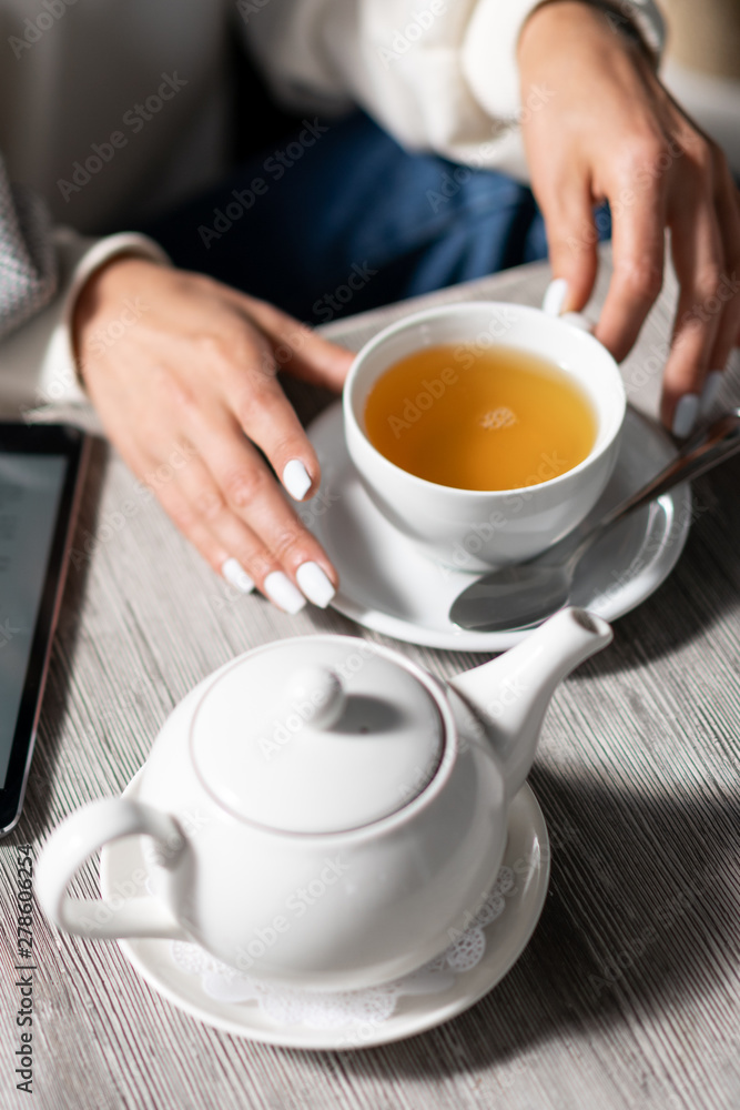 girl in sweater drinking tea in cafe. On table in restaurant is cup of tea and teapot. Cup of tea in hand girl girl in sweater drinking tea in cafe. On table in restaurant is cup of tea and teapot. Cup of tea in hand girl