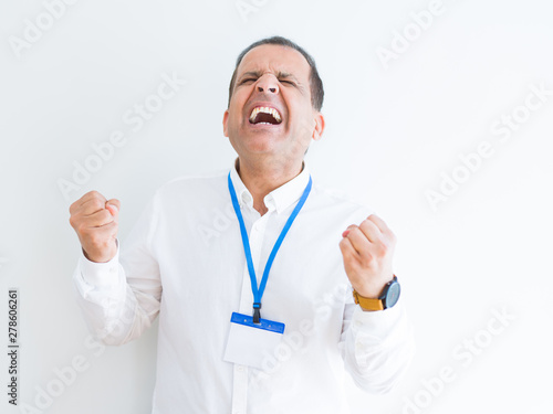 Middle age business man wearing ID card over white background very happy and excited doing winner gesture with arms raised, smiling and screaming for success. Celebration concept. © Krakenimages.com