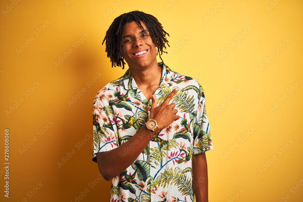 Afro man with dreadlocks on vacation wearing summer shirt over isolated yellow background cheerful with a smile of face pointing with hand and finger up to the side with happy and natural expression Afro man with dreadlocks on vacation wearing summer shirt over isolated yellow background cheerful with a smile of face pointing with hand and finger up to the side with happy and natural expression