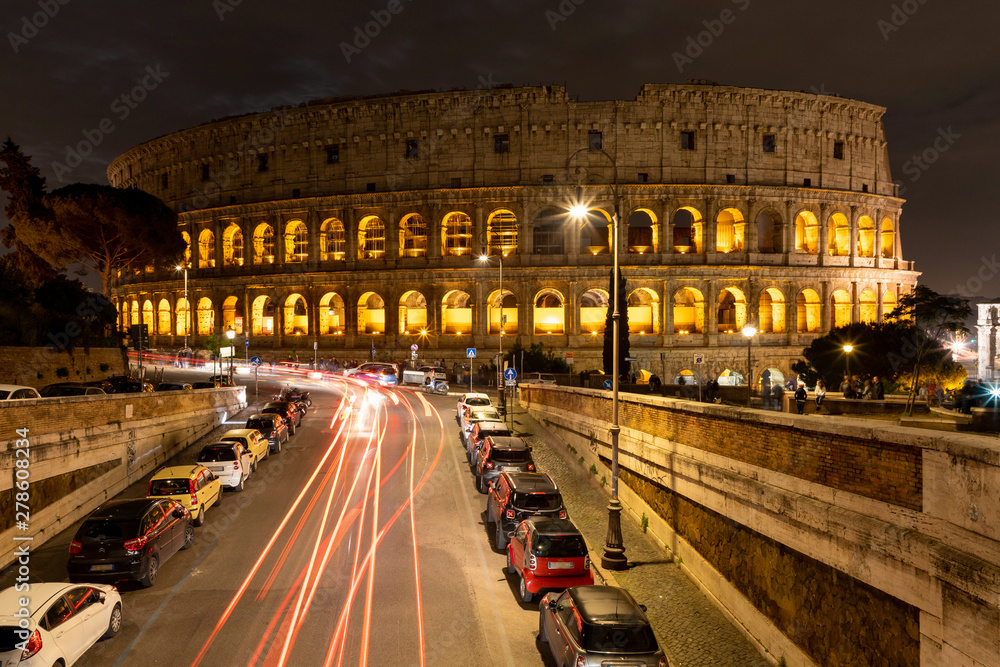 View of the night Colosseum, the road with passing cars. Rome, Italy.