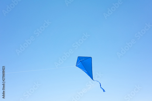 A blue kite soars in a cloudless sky. The concept of freedom, summer hobbies, entertainment in nature. Minimalism, space for text, shades of blue. photo