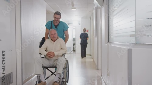 Male Orderly Pushing Senior Male Patient Being Discharged From Hospital In Wheelchair photo