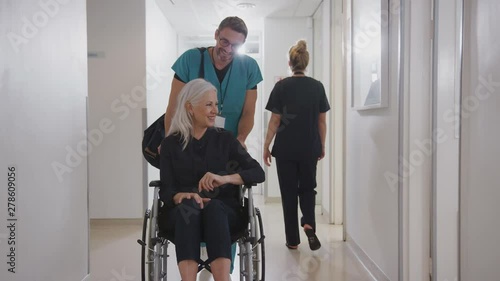 Male Orderly Pushing Senior Female Patient Being Discharged From Hospital In Wheelchair photo