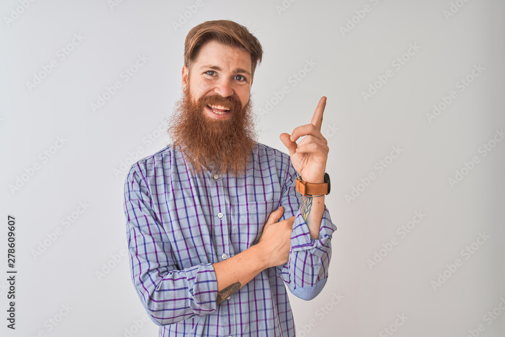 Naklejka premium Young redhead irish man wearing casual shirt standing over isolated white background with a big smile on face, pointing with hand and finger to the side looking at the camera.