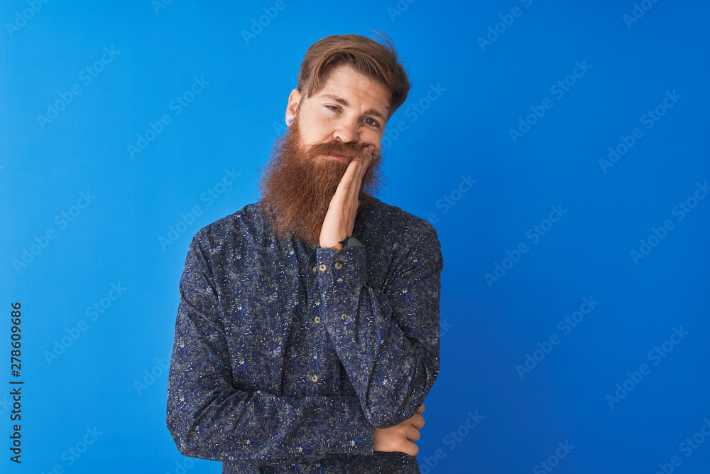 Young redhead irish man wearing floral summer shirt standing over isolated blue background thinking looking tired and bored with depression problems with crossed arms.