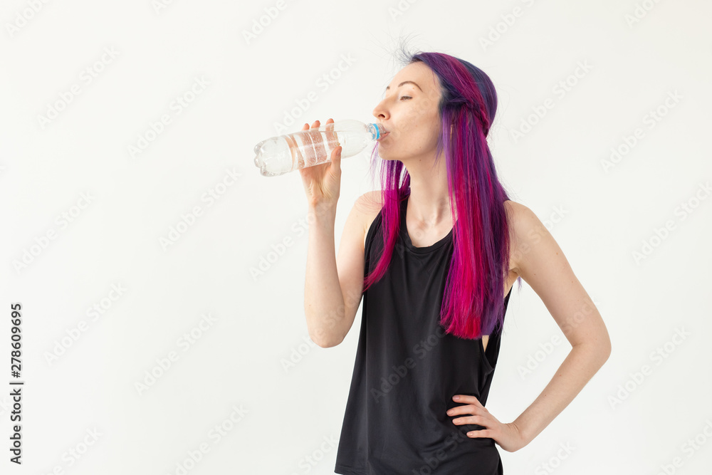 Young girl hipster with colored hair drinks water from a bottle after intense physical training in the gym. The concept of thirst and water balance of the body. White background with copy space Young girl hipster with colored hair drinks water from a bottle after intense physical training in the gym. The concept of thirst and water balance of the body. White background with copy space