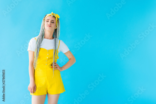 sad girl with dreadlocks and hand on hip isolated on turquoise