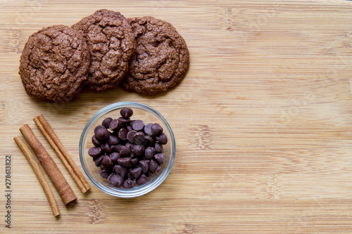 Chocolate chip brownie cookies with cinnamon displayed on a wooden cutting board; warm homemade chocolate cookies beside ingredients of cinnamon and chocolate chips