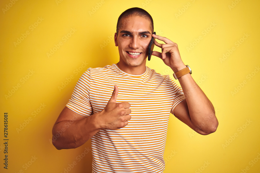 Young handsome man talking using smartphone over yellow isolated background happy with big smile doing ok sign, thumb up with fingers, excellent sign Young handsome man talking using smartphone over yellow isolated background happy with big smile doing ok sign, thumb up with fingers, excellent sign