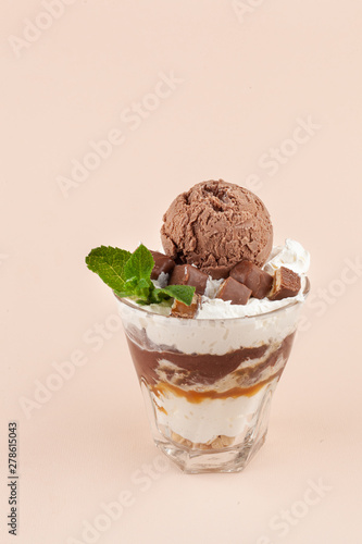 Layered ice cream dessert with twicks, caramel topping and whipped cream, isolated on pastel background photo