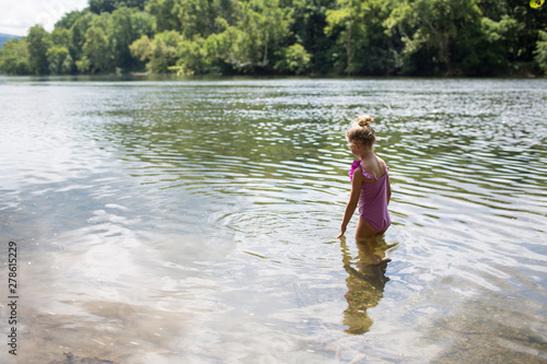 Rear view of Blonde Little Girl Walking into Lake with Trees Behind photo