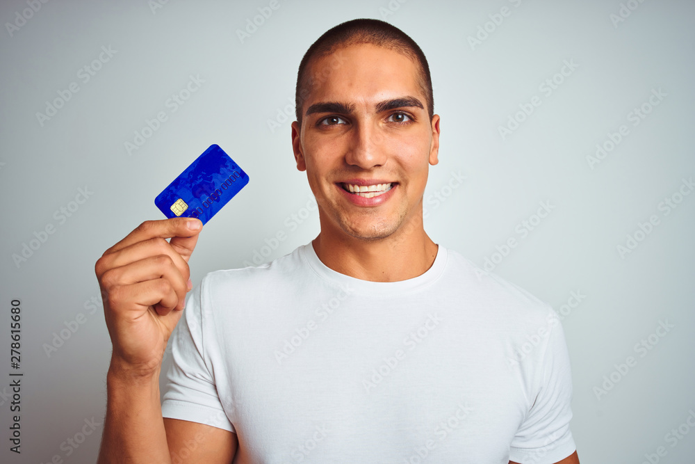 Young handsome man holding credit card over white isolated background with a happy face standing and smiling with a confident smile showing teeth Young handsome man holding credit card over white isolated background with a happy face standing and smiling with a confident smile showing teeth