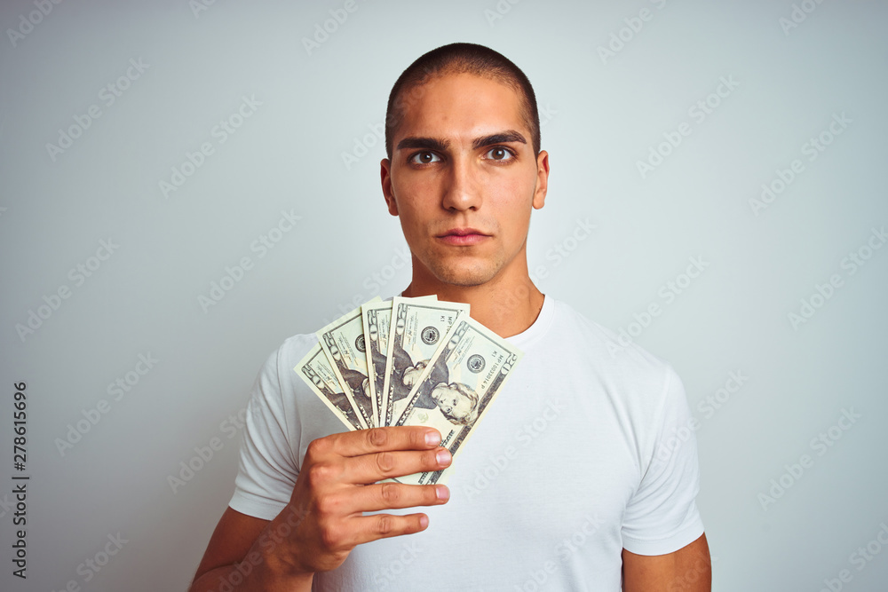 Young handsome man holding dollars over white isolated background with a confident expression on smart face thinking serious Young handsome man holding dollars over white isolated background with a confident expression on smart face thinking serious