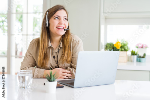 Beautiful young operator woman working with laptop and wearing headseat looking away to side with smile on face, natural expression. Laughing confident.