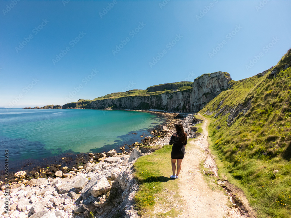 Young woman walking on path near Coast of Atlantic Ocean and Carrick Rede Rope Bridge 