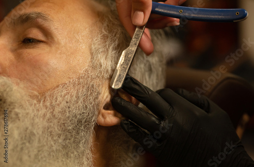 Master cuts hair and beard of men in the barbershop, hairdresser makes hairstyle for a old man