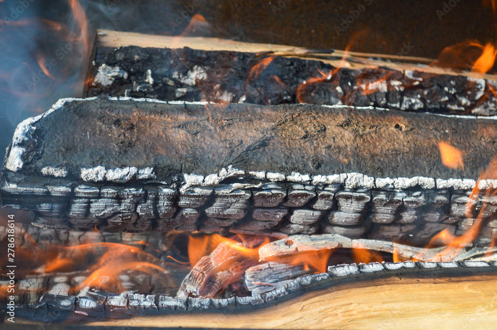 Wooden burning hot charred planks of wood logs in a fire with tongues of fire and smoke. Texture, background Wooden burning hot charred planks of wood logs in a fire with tongues of fire and smoke. Texture, background