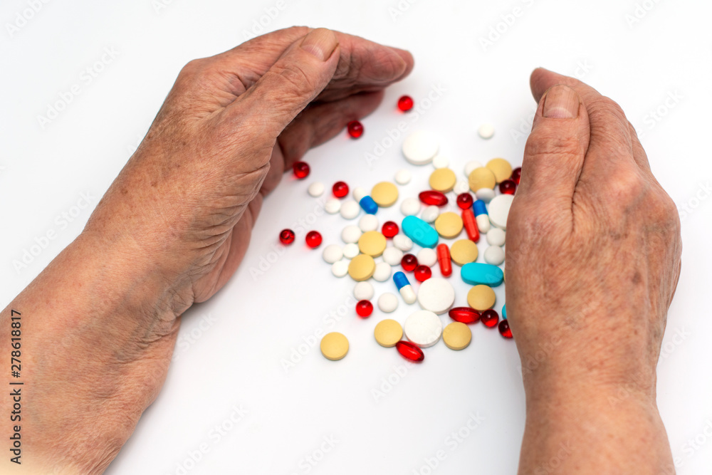 Old hands hold multicolored medical pills and tablets for ingestion from diseases on a white background. Old hands hold multicolored medical pills and tablets for ingestion from diseases on a white background.