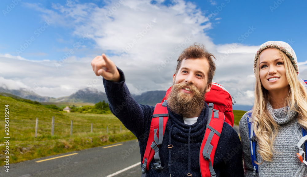 adventure, travel, tourism, hike and people concept - couple of travelers with backpacks over connemara road background adventure, travel, tourism, hike and people concept - couple of travelers with backpacks over connemara road background