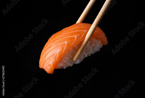 Traditional japanese nigiri sushi with salmon placed between chopsticks, separated on black background photo