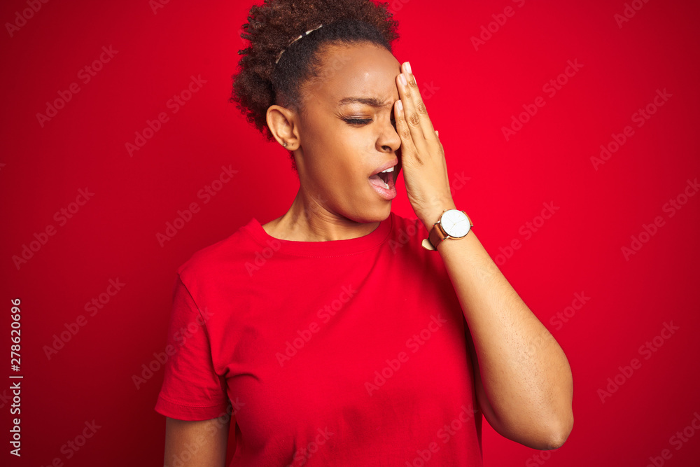 Young beautiful african american woman with afro hair over isolated red background Yawning tired covering half face, eye and mouth with hand. Face hurts in pain. Young beautiful african american woman with afro hair over isolated red background Yawning tired covering half face, eye and mouth with hand. Face hurts in pain.