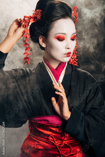 Valokuva geisha in black kimono with red flowers in hair gesturing on black background wi