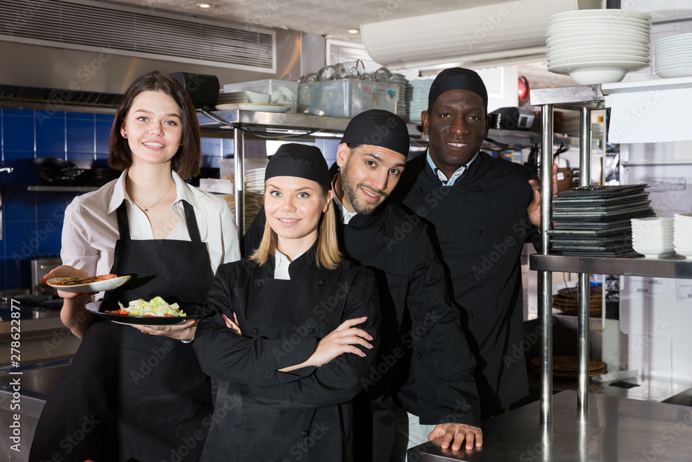 Portrait of command of cooks and woman waiter who are posing together on kitchen