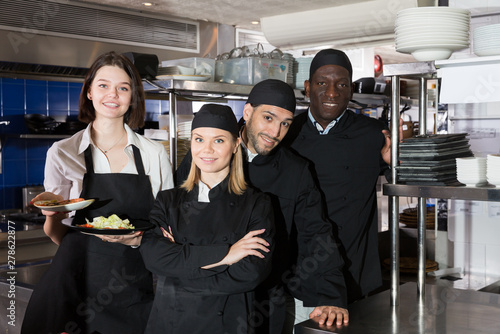 Portrait of command of cooks and woman waiter who are posing together on kitchen