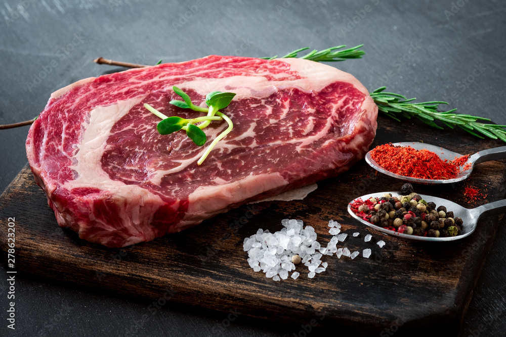 Fresh raw Rib eye Steak with seasonings and red pepper on cutting Board on grey background, close up