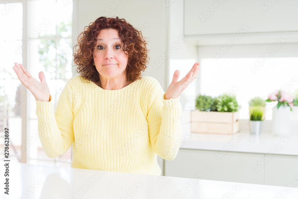 Beautiful senior woman wearing yellow sweater clueless and confused expression with arms and hands raised. Doubt concept.