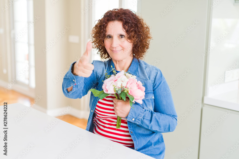 Senior woman holding beautiul bouquet of pink flowers pointing with finger to the camera and to you, hand sign, positive and confident gesture from the front Senior woman holding beautiul bouquet of pink flowers pointing with finger to the camera and to you, hand sign, positive and confident gesture from the front