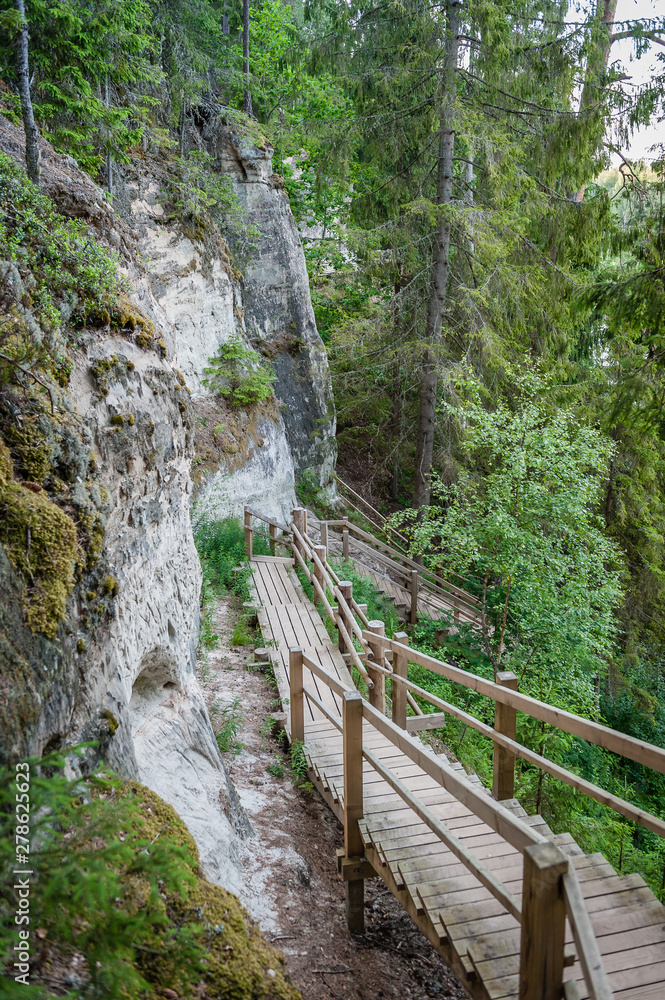 Tourist trail with wooden pathwalk and stairs near sandstone cliffs. The cliff of Sietiniezis, Latvia. Gauja National Park. Tourist trail with wooden pathwalk and stairs near sandstone cliffs. The cliff of Sietiniezis, Latvia. Gauja National Park.