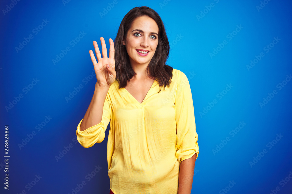 Fototapeta premium Young beautiful woman wearing yellow t-shirt standing over blue isolated background showing and pointing up with fingers number four while smiling confident and happy.