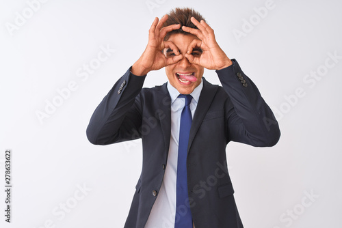 Young handsome businessman wearing suit standing over isolated white background doing ok gesture like binoculars sticking tongue out, eyes looking through fingers. Crazy expression.